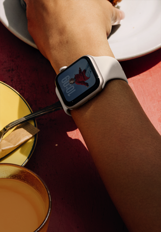 A person's arm grabbing breakfast food, Apple Watch SE 3 on wrist, Starlight aluminium case, always-on display, portrait of a person on watch face, starlight Sport Band