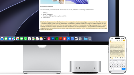 Mac mini front, tucked under Studio Display, an iPhone sits to the right of the device and the display, text selected with cut, copy, paste and AutoFill commands above on iPhone matches highlighted text on display, showcasing Universal Clipboard
