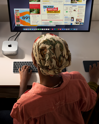 A person typing at a desk with a Mac mini, Studio Display connected, Magic Keyboard, Magic Trackpad, various items