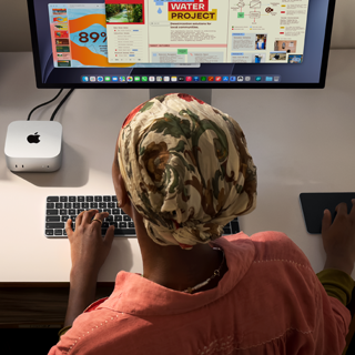 A person typing at a desk with a Mac mini, Studio Display connected, Magic Keyboard, Magic Trackpad, various items