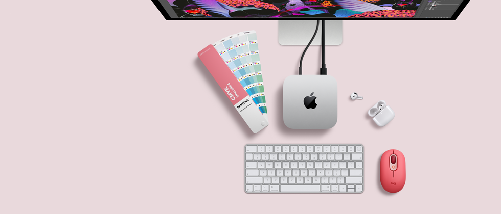 Mac mini, top, silver aluminium, rounded corners, glossy black Apple logo centred, connected by cord, Studio Display partially visible on top, AirPods 4, open, Pantone colour swatches, and red Logitech keyboard and mouse