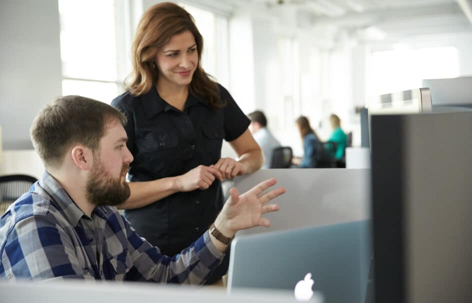 Colleagues in an office, discussing over a computer.