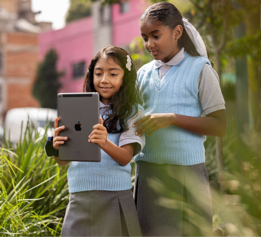 Two younger pupils using the built-in camera on their iPad device outside of the classroom, to take part in practical learning beyond the classroom.