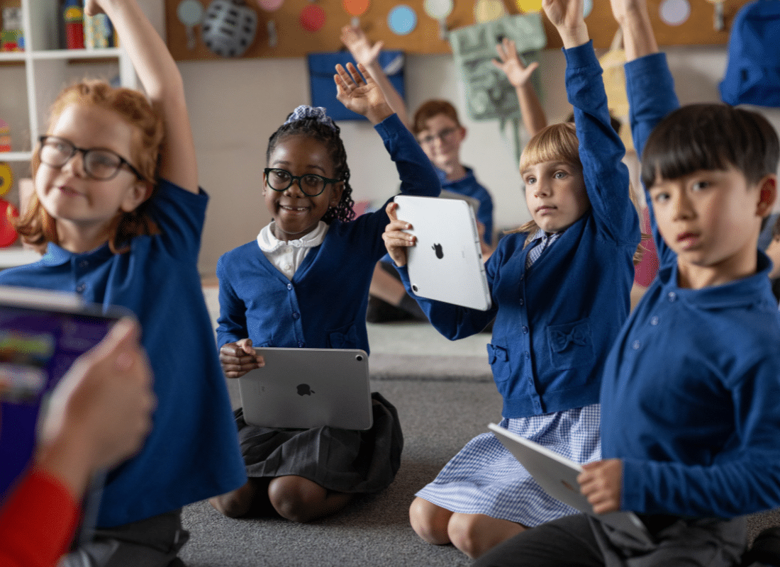 Students sat amongst each other on the floor using iPad, raising their hands to answer a question