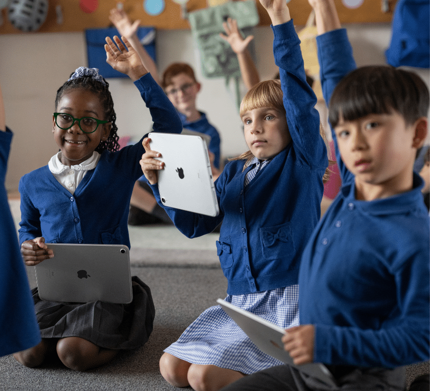 Students sat amongst each other on the floor using iPad, raising their hands to answer a question